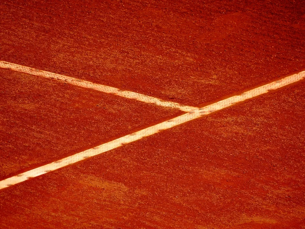 Detalle del cruce de dos líneas blancas sobre una superficie de tierra batida