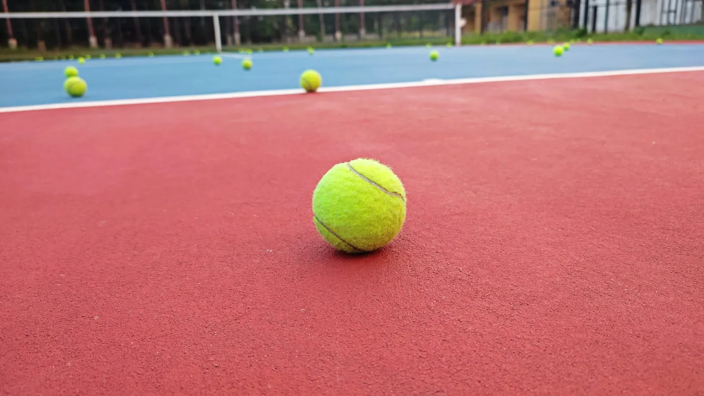 Pelotas de tenis repartidas por una pista de superficie sintética roja y azul