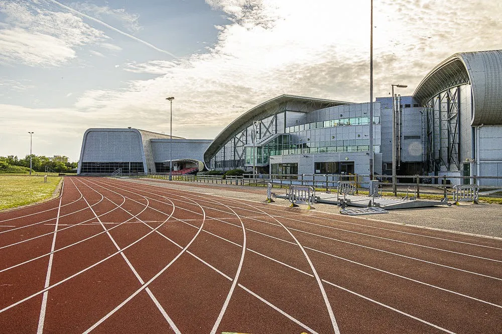 Curva de una pista de atletismo con calles marcadas junto a un edificio deportivo moderno