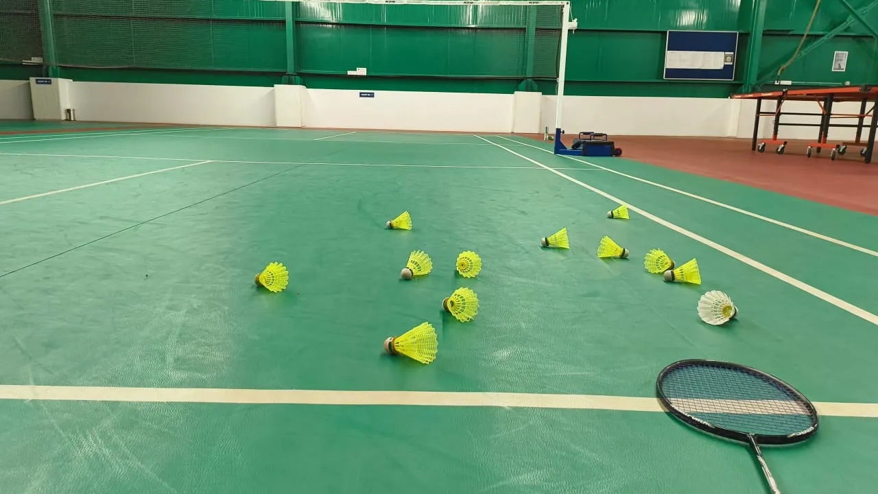 Pista cubierta de bádminton con conos y volantes repartidos por el suelo junto a una raqueta