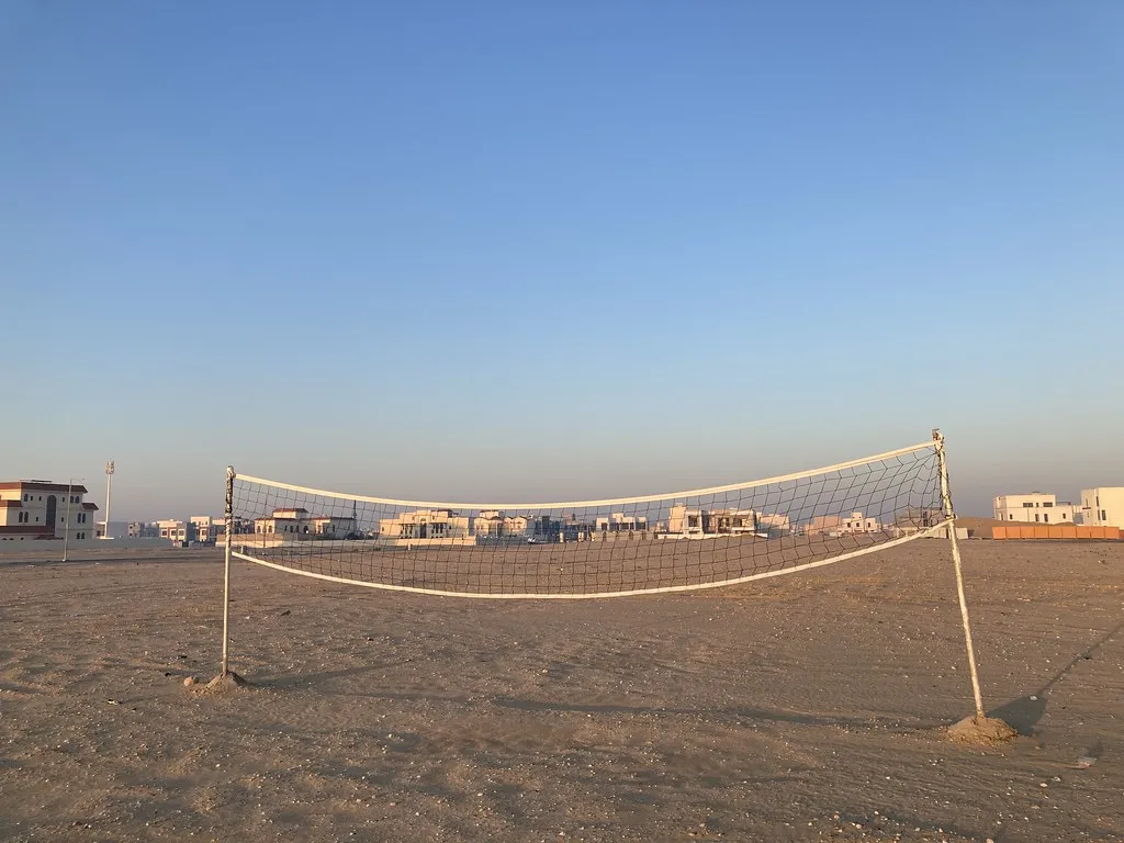 Red de voleibol montada sobre arena al atardecer, con edificios bajos al fondo