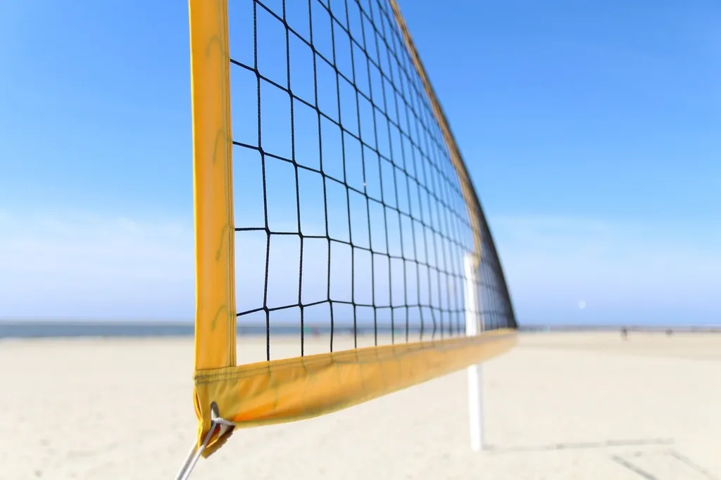 Primer plano de la banda superior de una red de voleibol tensada sobre la arena